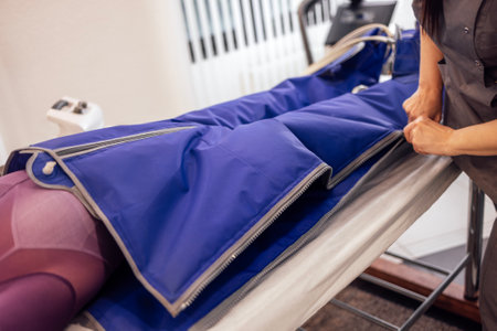 Young attractive woman lies with her hands behind her head in a special suit during pressotherapy. Hardware lymphatic drainage massage in a spa salon or clinic. Non surgical hardware cosmetology.の写真素材
