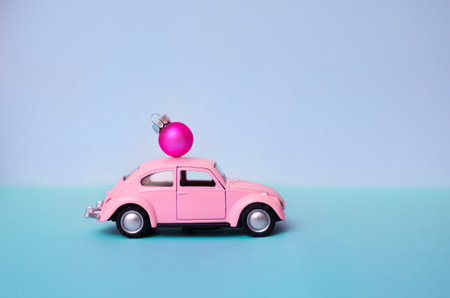 Pink toy car with a Christmas ball on the roof. Miniature automobile with a Christmas decoration on...