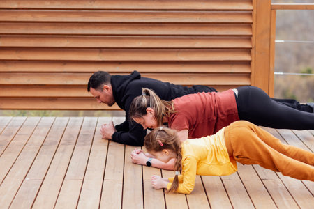 Happy family are stretching outdoors. Attractive mom, handsome dad and cute daughter doing sport exercises. Young couple and their kid are training in the park. Smiling man, woman and girl go in for sports.の写真素材