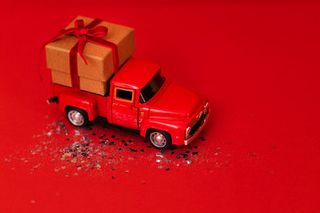 Red toy truck with craft gift box and red bow in its trunk. Miniature car with Christmas decoration...