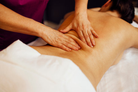 Happy young caucasian girl getting back massage in spa salon. Neat hands of female masseuse with orange manicure. Beautiful smiling woman gets relaxation. Copy space.の写真素材