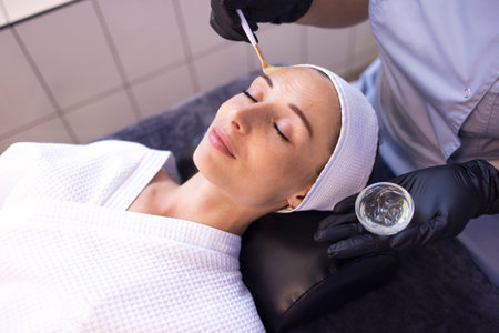 Beautiful caucasian girl is doing a cosmetic procedure. The beauty master applies a rejuvenating mask to the clients face. skin lifting. The concept of beauty and skincare. copy place. close up.の写真素材