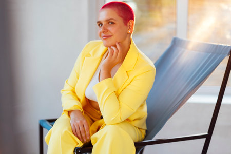 Beautiful relaxed woman in yellow suit and red shot hair while resting on weekend day at homeの写真素材