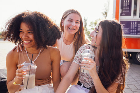 Close up of three teenage girls in casual clothes drinking tasty lemonade on the go. Happy female...