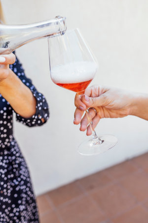 A young woman pours pink champagne from a transparent bottle. Close up of a female hand with a neat...
