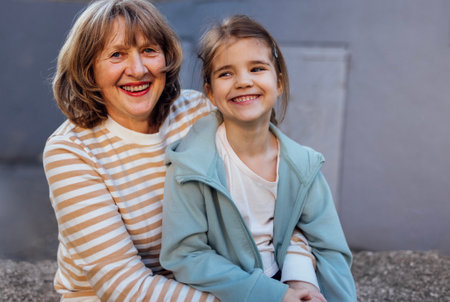 Little girl hugging smiling middle aged woman. Cute female kid and her grandmother enjoy walking outdoors. Granny and her granddaughter having great time together. Joyful meetings of family members.の写真素材