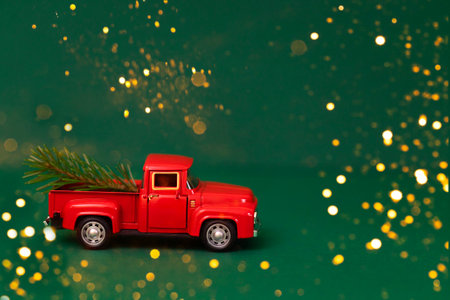 Red toy truck with Christmas fir branch in its trunk. Miniature car with Christmas decoration on green background. Bright backdrop with sparkles and confetti. New Year holiday concept.の写真素材