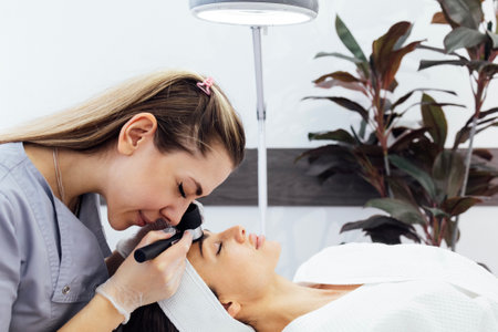 Doctor dermatologist examines skin of client face of beauty salon with a dermatological lens. Dermatoscopy. Free space for text.の写真素材