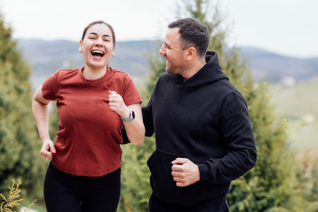 Smiling attractive woman and handsome man jogging in the summertime. Happy young couple doing sport. Laughing athletes running through the park. Healthy sports people training in the morning.の写真素材