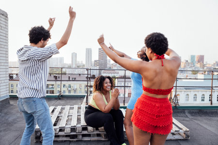 Three charming African American girls and mixed race guys are dancing on the roof of multi-storey...
