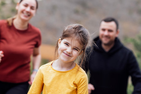 Happy family jogging in the summertime. Smiling young couple with their cute daughter doing sport. Man, woman and little girl training in the morning. Sports people and kids running through the park.の写真素材