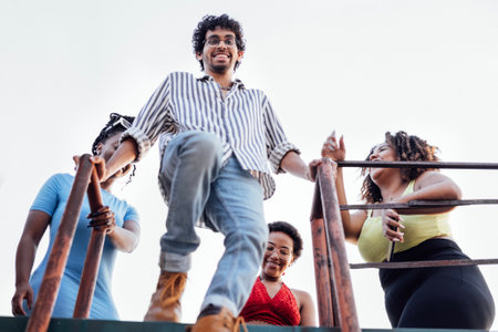 Four cheerful multiethnic friends descend the iron ladder from the roof of the house. Charming...
