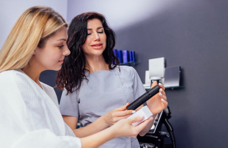 Pretty caucasian beautician communicates with her female client. Beauty master holds cosmetics in...