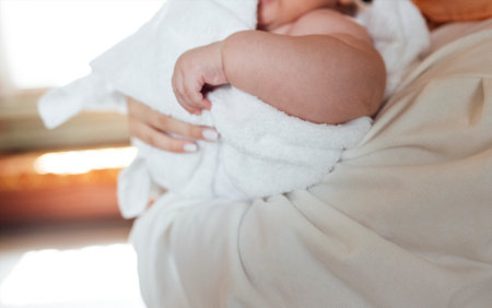 Sweet cute baby sits on the bed next to his mom and plays after bath. Light color bedroom interiorの写真素材