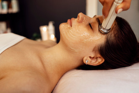 Closeup of face of beautiful relaxing girl undergoing hardware cosmetology procedure in spa. Cream...