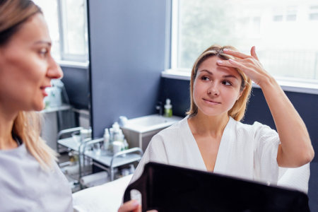 Doctor checking woman face skin in cosmetology clinic before plastic surgery. Surgeon or beautician touching woman face. Female client with facial lines looks at herself in the mirror. copy spaceの写真素材