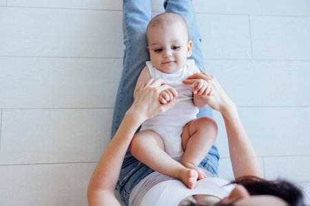 Young beautiful mother hugging her cute baby on cheek. White brunette touches her smiling child with her face. Pretty infant in a white bodysuit with his mom on a light background. Motherhood concept.の写真素材