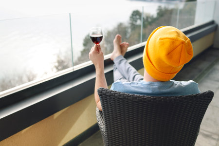 Young man in gray casual clothes and yellow hat sits on wicker chair with his bare feet outstretched...