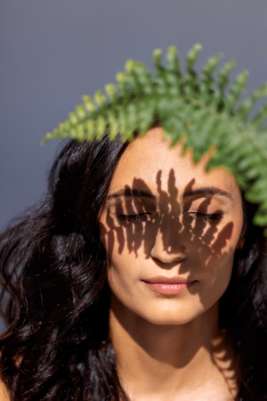 A close-up beauty portrait of a young attractive woman with closed eyes and a green leaf. A...