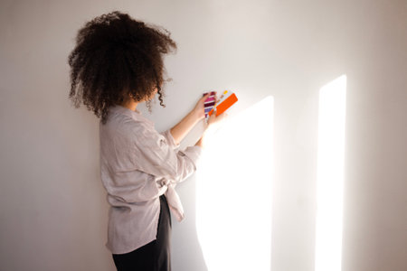 A beautiful smiling African woman in casual clothes holds color palettes. A charming young girl of mixed race chooses the color of the walls of the house. Renovation in the apartment.の写真素材