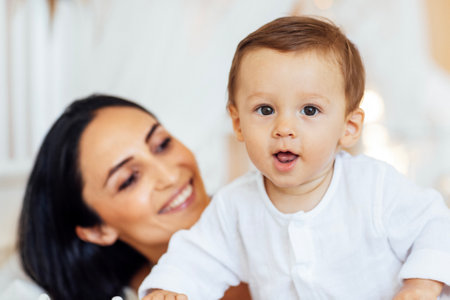 A beautiful young woman in a white top and black leggings holds her little son in a black shorts. An adorable mom hugs her sweet baby. Family look.の写真素材