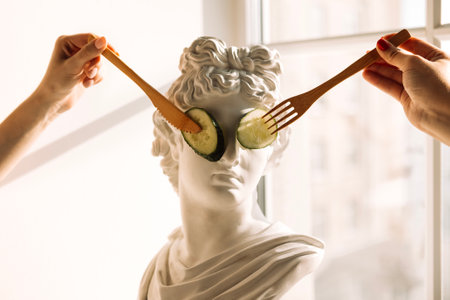 A plaster copy of an antique bust of a young man with cucumber slices in front of his eyes. Two...