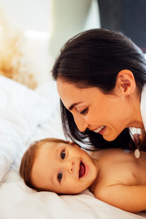 A close-up portrait of a young smiling woman and her sweet baby. A charming mom is playing with her...