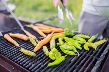 Close-up of a vegetarian barbecue and a cooking man. Tasty fried peppers and carrots on the grill. Vegetables are cooked on coals on the bars in the open air. Weekend lunch.の写真素材
