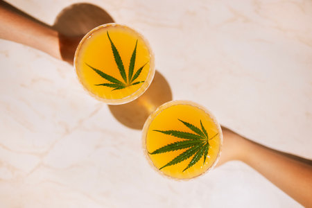 Two outstretched hands with elegant glasses with delicious cocktails with cannabis leaves on the marble surface of the table. Tasty healthy juice with hemp on a background with neon light. Top view.の写真素材