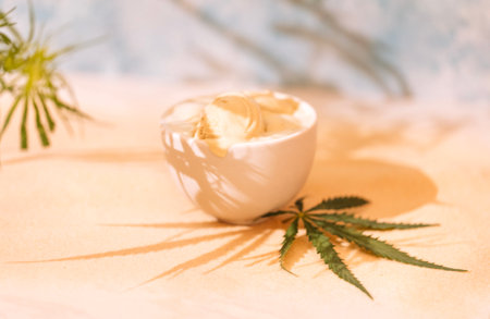 A white ceramic bowl with delicious ice cream and a cannabis leaf. A sweet treat with hemp on golden sand. Tasty cold yummy. Organic food and health.の写真素材