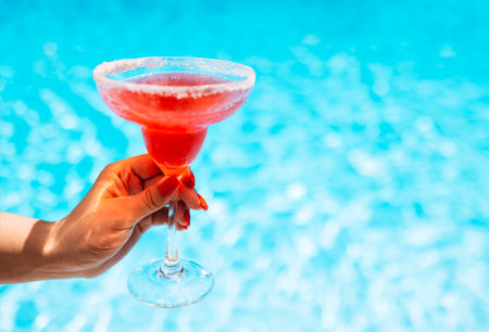 A female hand with a neat manicure reaches for an elegant glass with long stem with a cocktail....