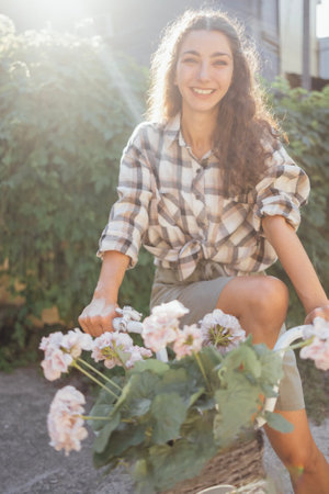 A young attractive woman in casual clothes is sitting on a bicycle in the garden. A charming curly-haired girl is smiling outdoors in the bright sunlight. A carefree cute female cyclist on the street.の写真素材