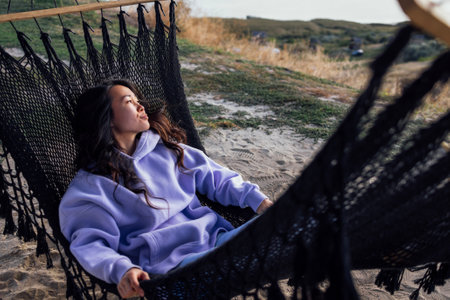 A young charming Asian woman lies in a hammock and looks at the mountains. A beautiful Korean woman...