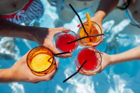 Close-up of female and male hands holding glasses with iced cocktails and clinking them. Friends...