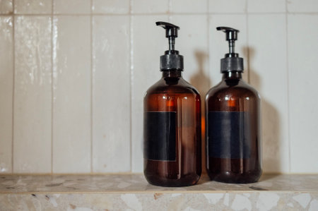 Close-up layouts with brown plastic bottles with dispensers in the bathroom. Mock-ups of shampoo or gel tubes with black empty labels on a background of tiles. Cosmetic products.の写真素材