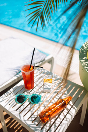 Sunscreens, sunglasses and a delicious chilled cocktail on the pool table. Mock-ups of cosmetics and lemonade next to the chaise longue. A delicious cooling drink on vacation at the hotel.の写真素材