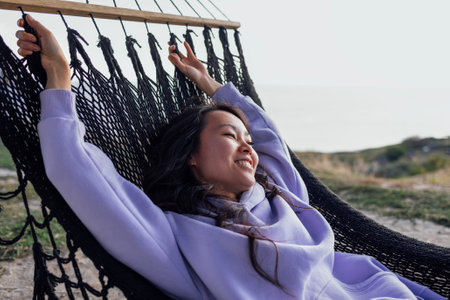 A young charming Asian woman lies in a hammock and looks at the mountains. A beautiful Korean woman...