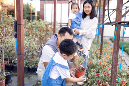 Asian couple with children choose garden plants. Korean man and his charming wife with cute children are buying green planters home. Young woman with little daughter, son and husband in plant nursery.の写真素材
