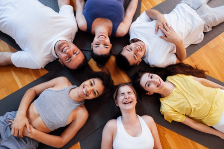 Multi-racial smiling people lie on mats after doing yoga at a fitness club. A group of young athletes relax and rest after physical exercises in the gym. Indoor training. Studio background.の写真素材