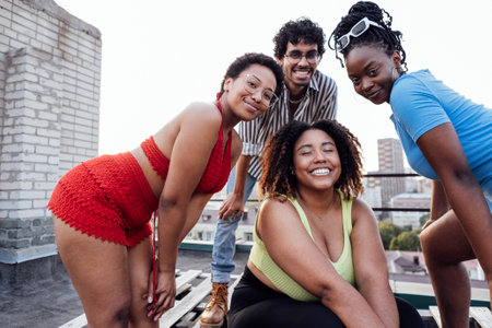 Four smiling mixed race friends standing and looking down at camera. Group of cheerful multiethnic people in casual clothes having fun together outdoors. Happy laughing man and women. Low angle view.の写真素材