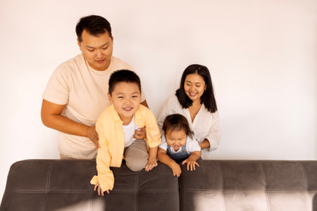 Happy Asian family at home. A Korean couple and their cute little kids on the sofa in the living room. Parents and their son and daughter pose together.の写真素材