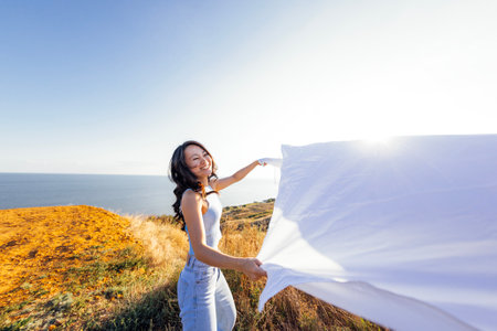 An attractive Asian woman laughs and holds an open sheet outdoors. A charming Korean woman enjoys nature. A beautiful girl is having fun.の写真素材