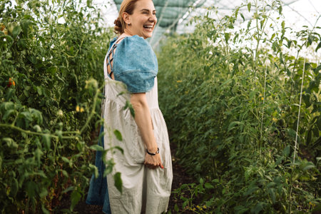 Closeup of a young attractive female farmer checking the ripe fruits of black tomatoes. A smiling charming woman in casual clothes works on an agricultural farm. Harvest time at the tomato plantation.の写真素材