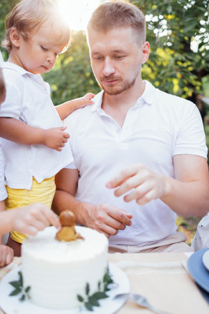 Young dad and toddler son look at sweet birthday cake outdoors. A man and a child are tasting a festive pie with a figurine of a lion cub decoration in the garden at home. Sunny day. Happy holiday.の写真素材