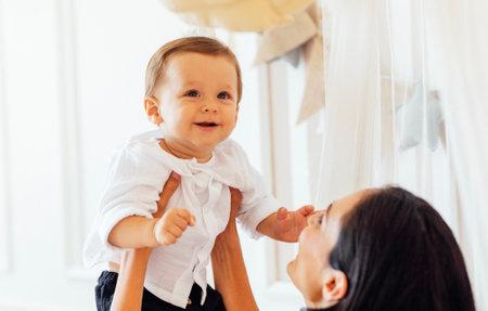 A young beautiful mom lifts her cute little boy in her arms. An attractive woman is playing with her...
