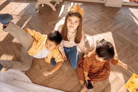 Cute children of different races play together. Asian sibling and caucasian girl are messing around in the bedroom on the floor. Small children have fun in the living room of the house. The concept of friendship and childhood.の写真素材