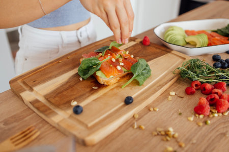 A woman's hands are carefully placing slices of fresh salmon on a piece of bread on the kitchen. The...
