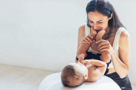 A young attractive woman kisses the feet of her little son. Adorable mom is playing with her cute boy. Mother and baby have fun together at home.の写真素材