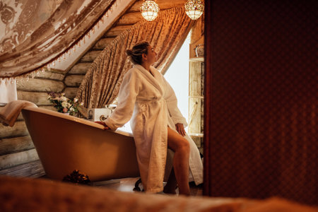 A young woman in a white bathrobe in the hotel bathroom. A charming girl is going to take a bath and enjoy a spa procedure. Vintage retro interior.の写真素材