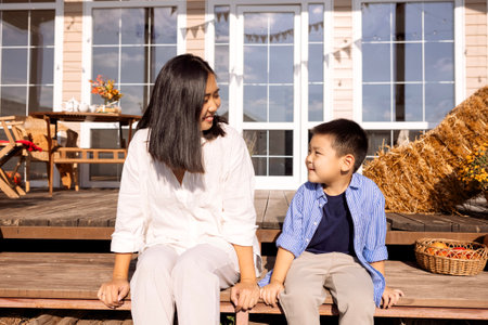An attractive young woman and her cute son are sitting in the backyard of the house. A charming mother and her little boy spend time together and enjoy a sunny day.の写真素材